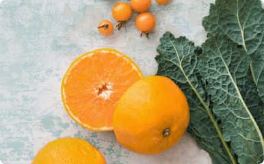 Orange split in half on a table with green kale and orange tomatoes.