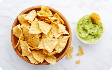 Tortilla chips in brown bowl with a guacamole dip next to it.